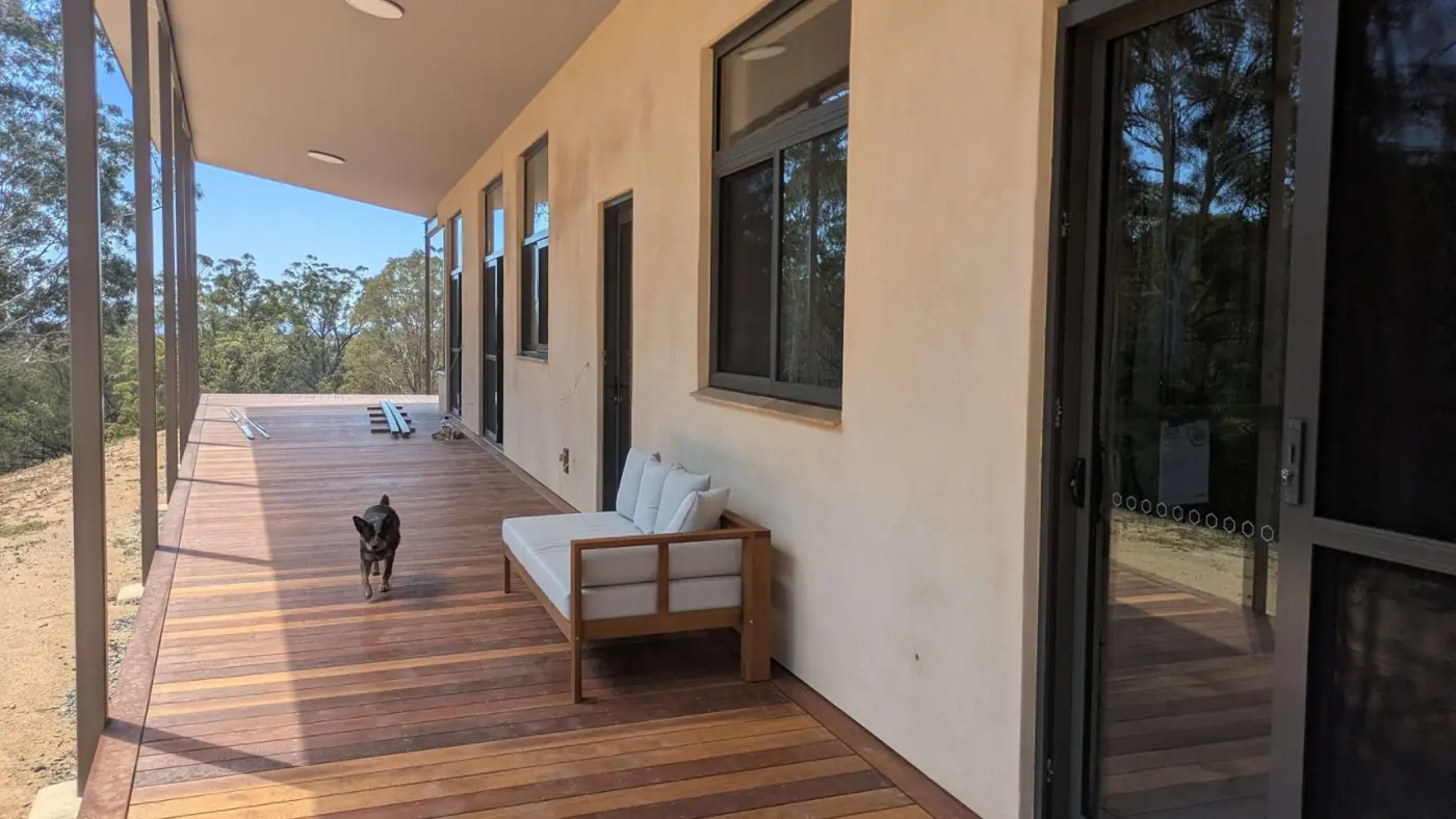 Rendered hempcrete verandah wall of a Respirabuilt home near Bega, with a timber deck, an outdoor lounge and a dog